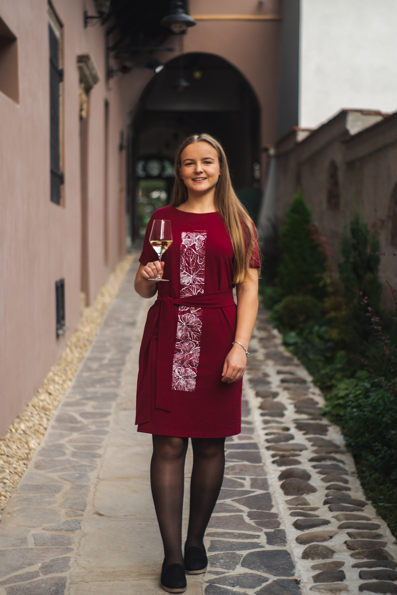 Bordové teplákové šaty In Vino s opaskom, modelka v ruke drží pohár bieleho vína