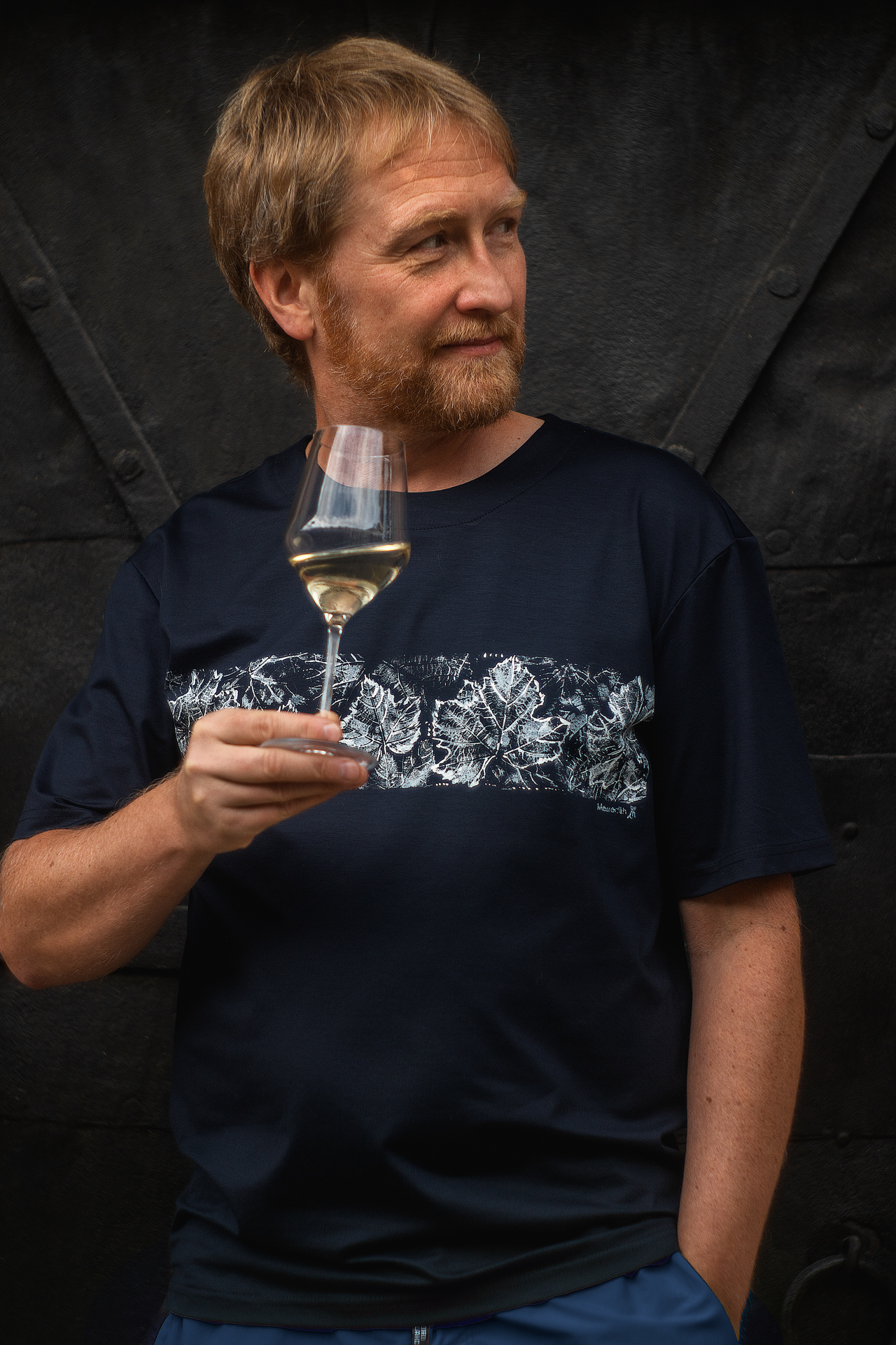 Tmavomodré pánske tričko In Vino s motívom viniča, model v ruke drží pohár bieleho vína